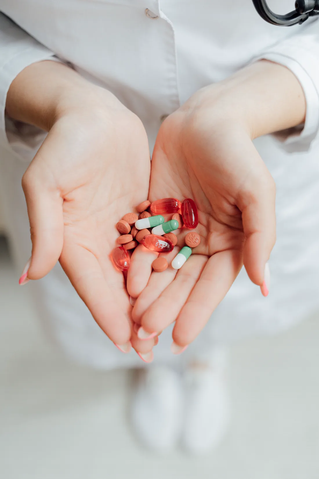 A pharmacist's cupped hands holding an assortment of tablets and capsules