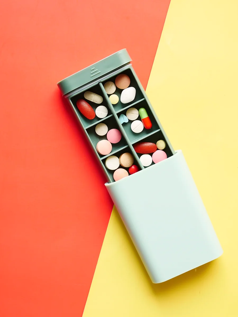 A mint pill organizer with doses sorted into compartments, on a bold red and yellow background